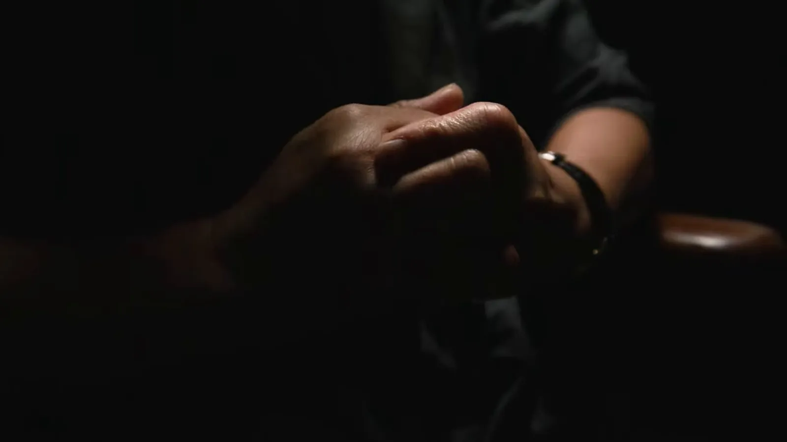 Clasped hands in a dim room, living with chronic pain after an injury